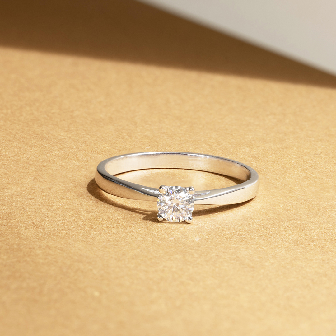 Bague en argent brillante avec un diamant carré au centre, présentée sur un fond doré, idéale pour une demande en mariage ou comme bijou élégant, mettant en valeur la beauté et la clarté du diamant.