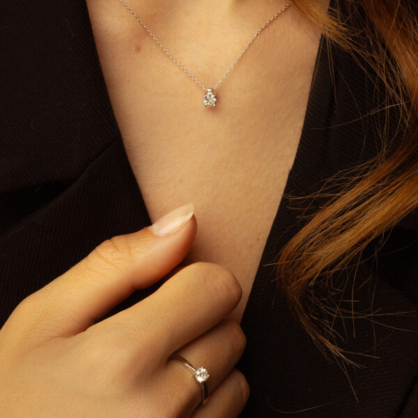 Collier délicat en argent avec un pendentif en diamant scintillant, porté par une main élégante. La main montre également une bague en argent ornée d'un brillant, mettant en valeur la sophistication et le style. Idéal pour des occasions spéciales ou un usage quotidien, ce bijou ajoute une touche de luxe et d'éclat à toute tenue.