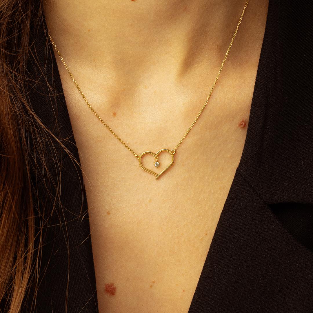 collier en or en forme de cœur avec un diamant, porté autour du cou, mettant en valeur l'élégance et la simplicité du bijou, parfait pour offrir en cadeau ou pour un style quotidien.