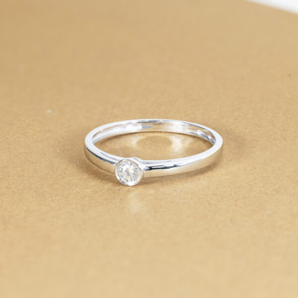 Bague en argent avec un diamant rond serti, modèle élégant et moderne, parfait pour les fiançailles ou un cadeau spécial. Présentée sur un fond doré pour mettre en valeur son éclat et sa brillance. Idéale pour un look raffiné et intemporel.