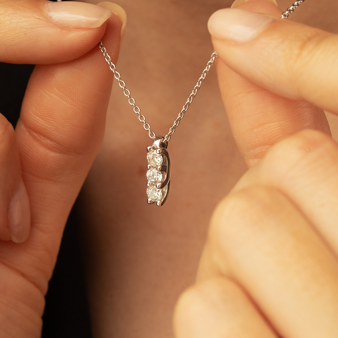 Pendentif en argent avec plusieurs diamants scintillants, porté pendant que des mains féminines tiennent délicatement la chaîne, mettant en valeur son élégance et son design moderne. Idéal pour les occasions spéciales ou un usage quotidien. Modèle + diamant.