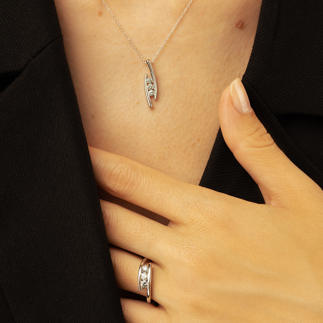Collier en argent avec un pendentif moderne et brillant, accompagné d'une bague en argent élégante. Le bijou met en valeur des diamants étincelants, accentuant le style chic et contemporain de la modèle. Idéal pour une occasion spéciale ou un usage quotidien, ce duo de bijoux incarne l'élégance minimaliste.