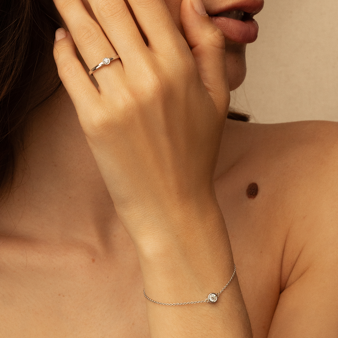 Une main féminine délicate portant une bague en argent avec un petit diamant et un bracelet fin en argent également décoré d'un diamant. L'image met en avant la beauté et l'élégance des accessoires de mode, le bracelet brillant et la bague sobre et raffinée. Idéal pour illustrer la bijouterie, la mode féminine et les tendances de style.