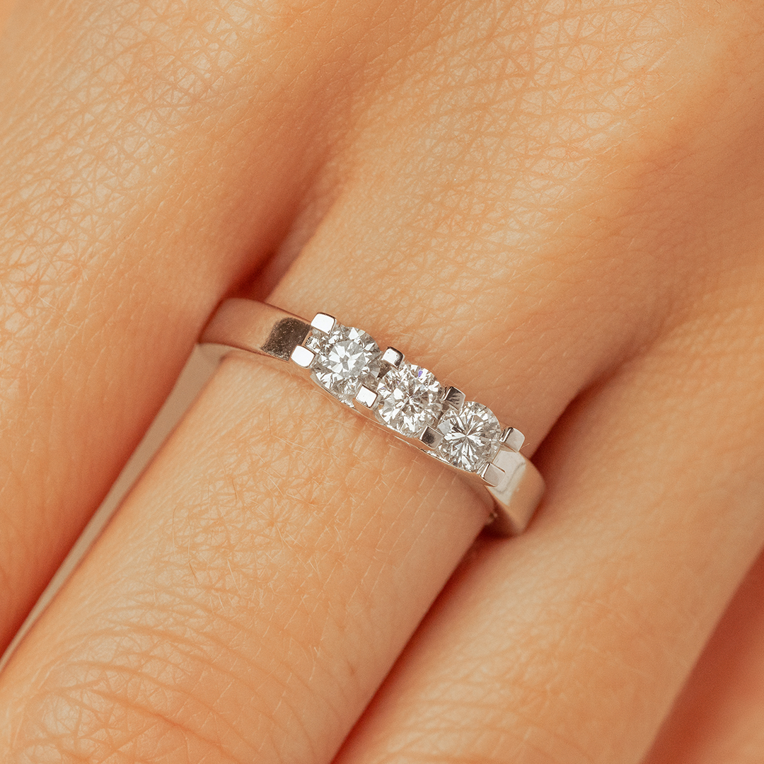 Bague en or blanc avec trois diamants ronds scintillants, portée sur un doigt, illustrant un design élégant et moderne, parfaite pour des occasions spéciales comme les fiançailles ou les anniversaires, mettant en valeur la brillance et le luxe.