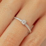 Bague en or blanc avec un diamant central scintillant et des petits diamants incrustés sur la bande, mettant en avant un design élégant et sophistiqué, idéale pour une proposition ou un cadeau spécial. Modèle + diamant.