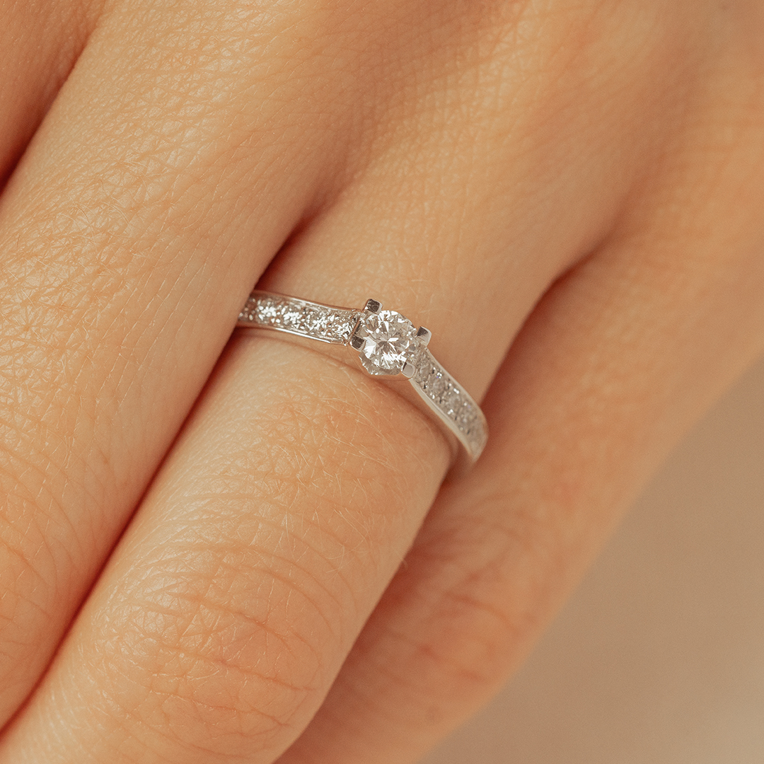 Bague en diamant élégante avec un design fin, mettant en valeur un diamant brillant au centre et des petits diamants sur la bande, positionnée sur un doigt humain. Parfaite pour une demande en mariage ou une occasion spéciale, ce modèle diamant reflecte sophistication et amour.