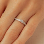 Bague de fiançailles en or blanc avec un diamant central éclatant et des diamants plus petits sur le band, portée sur une main féminine. Cette pièce de joaillerie raffinée est parfaite pour symboliser l'amour et l'engagement, ajoutant une touche de brillance et d'élégance à toute tenue.
