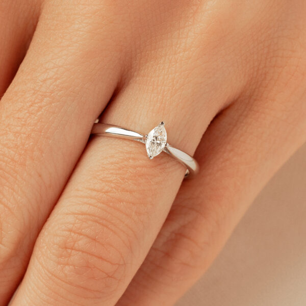 Bague de fiançailles en or blanc avec un diamant en taille marquise, posée délicatement sur un doigt, mettant en avant le design élégant et moderne, idéale pour une demande en mariage ou pour un bijou polyvalent du quotidien.
