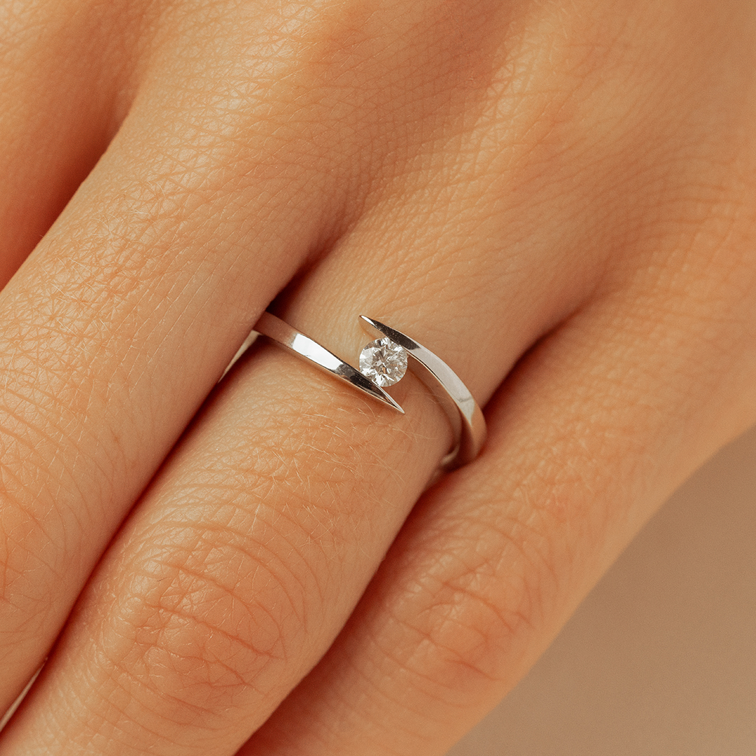 Bague en argent moderne avec un design minimaliste, mettant en valeur un diamant brillant, portée sur une main aux doigts légèrement ridés, symbolisant l'élégance et la simplicité. Idéale pour des occasions spéciales ou pour un usage quotidien.