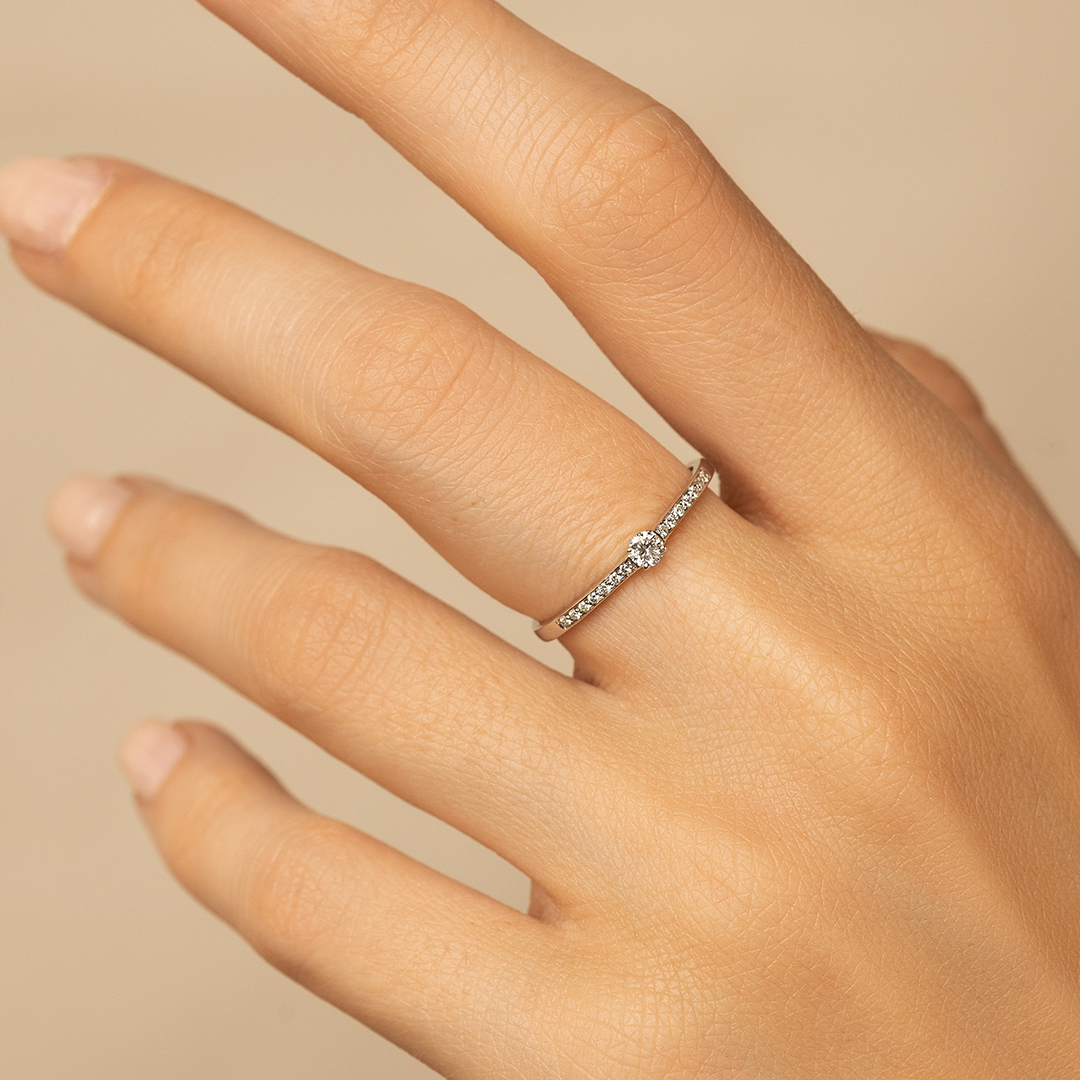 Bague élégante en or avec un diamant central et des diamants en pavé, portée sur un doigt délicat, mise en valeur par une main légèrement inclinée. Idéale pour les fiançailles ou les occasions spéciales, cette bague combine sophistication et brillance. Modèle + diamant.