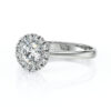 Bague en or blanc avec un diamant central entouré de diamants plus petits, style halo, mettant en valeur l'éclat et la brillance, idéale pour les fiançailles ou les occasions spéciales.