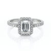Bague en diamant avec un motif émeraude en centre, entouré de petites pierres scintillantes sur un anneau en or blanc, illustrant l'élégance et le luxe parfaits pour une demande en mariage ou une occasion spéciale. Modèle + diamant.