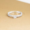 Bague en or blanc avec un diamant au centre et des petits diamants sur les côtés, idéale pour des fiançailles ou une alliance. Style élégant et moderne avec un design délicat, mettant en valeur la brillance du diamant principal, ajoutant une touche sophistiquée à toute occasion spéciale. Modèle + diamant.