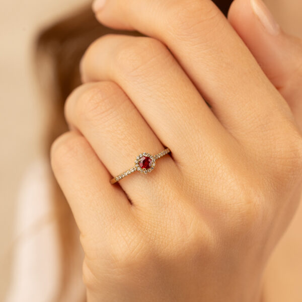 Bague en or jaune ornée d'un rubis central entouré de diamants, mise en valeur sur une main délicate, parfaite pour une occasion spéciale ou un cadeau romantique.
