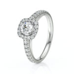 Bague en or blanc ornée d'un diamant central brillant, entouré de petits diamants en halo, avec une bande délicate en pierres précieuses. Modèle élégant et raffiné, parfait pour une demande en mariage ou une occasion spéciale.