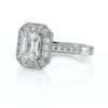 Bague en or blanc ornée d'un diamant taille émeraude au centre, entouré de pierres précieuses scintillantes, avec un design vintage élégant et un sertissage en pavé, parfaite pour une demande en mariage ou un cadeau spécial.