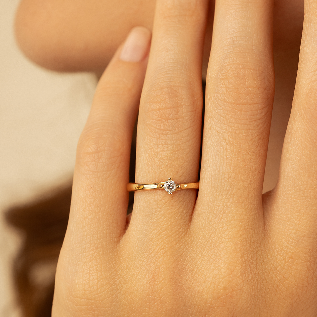 Bague en or avec un diamant central éclatant, mise en scène sur le doigt d'une femme. Cette élégante bague est parfaite pour les fiançailles ou comme bijou précieux, représentant le luxe et l'amour.