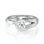 Bague élégante en or blanc avec un design moderne, présentant un diamant rond brillant au centre, entouré d'un cadre ondulé, symbole d'amour et d'engagement. Parfaite pour des fiançailles ou un cadeau romantique, cette bague allie sophistication et éclat, idéale pour les occasions spéciales.