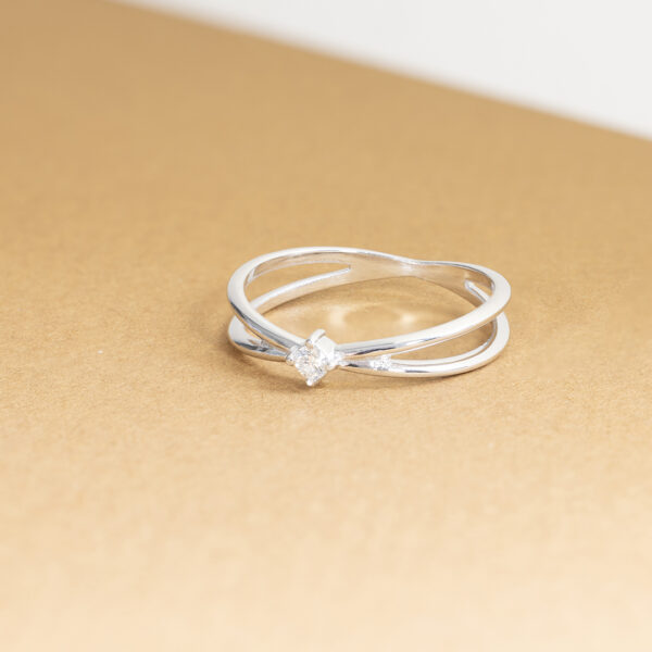 Bague en argent au design entrelacé, ornée d'un diamant brillant, sur un fond en papier doré. Idéale pour les fiançailles ou comme bijou tendance. Ce modèle élégant et unique met en valeur la beauté des diamants et le savoir-faire artisanal.