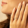 Femme souriante avec un élégant anneau en diamant sur son doigt, mettant en valeur une manucure soignée et des traits doux. Ce bijou chic est parfait pour les occasions spéciales ou un usage quotidien, offrant une touche de raffinement. Modèle avec diamant.