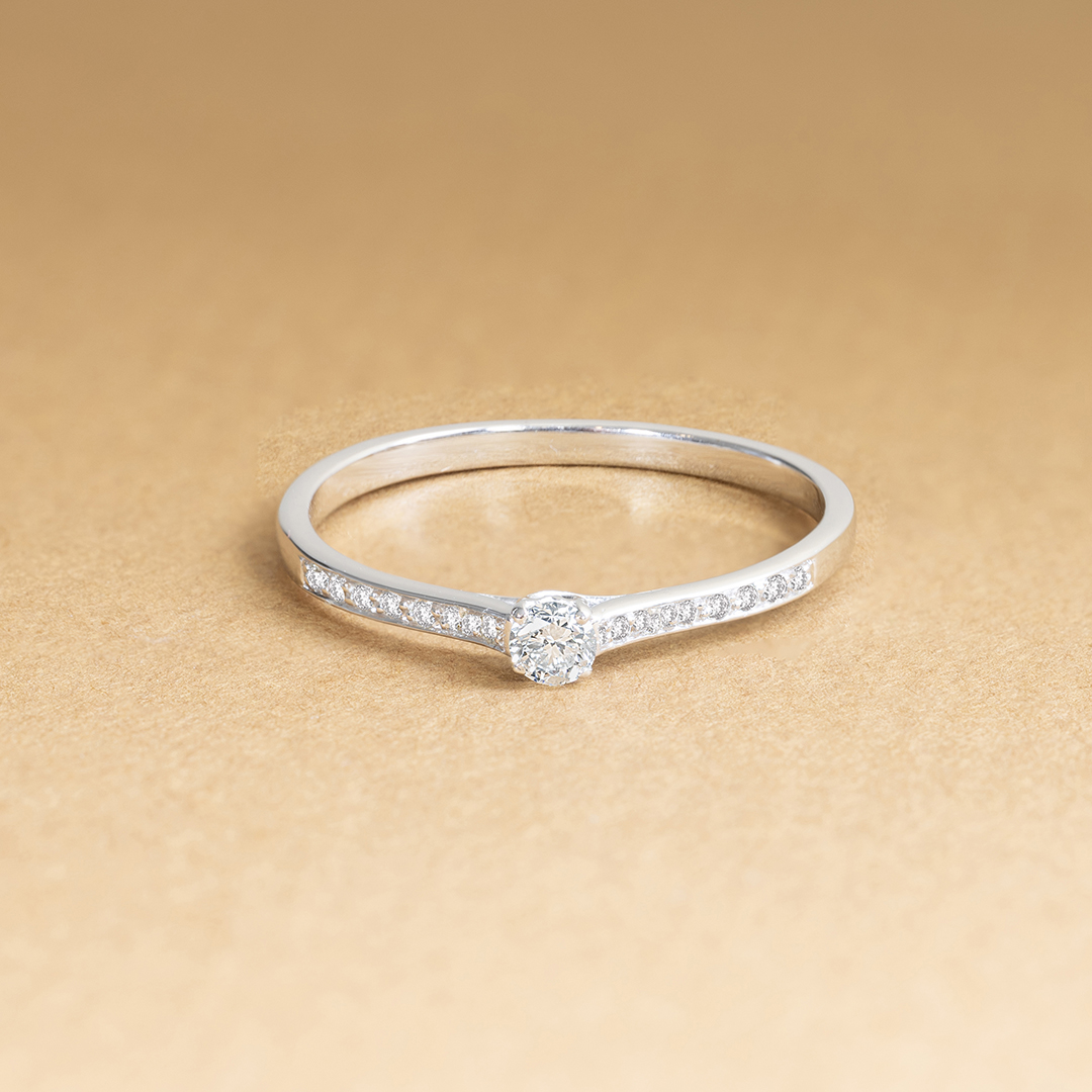 Bague en or blanc avec un diamant central entouré de petits diamants, élégante et discrète, modèle de bague de fiançailles classique et raffinée, idéale pour un moment spécial ou une demande en mariage, mettant en avant la brillance des diamants et la finesse du design.