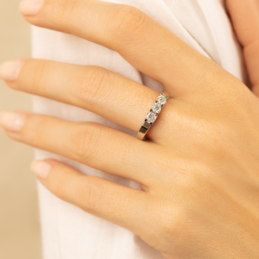 Bague en or blanc avec trois diamants brillants et un design élégant, portée sur la main d'une personne. Parfaite pour un engagement ou une occasion spéciale, mettant en valeur la finesse et le luxe de la joaillerie contemporaine. Bague diamant moderne.