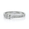 Une élégante bague en or blanc avec un design intemporel, mettant en valeur un diamant central entouré de diamants plus petits sur le côté, idéale pour les fiançailles ou les occasions spéciales. Bague diamant chic et raffinée.