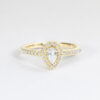 Bague en or jaune ornée d'un diamant en forme de poire, entouré de petits diamants ronds en pavé, créant un élégant design classique. Cette bague est parfaite comme bague de fiançailles ou bijou de luxe, mettant en avant le charme et l'éclat du diamant central tout en ajoutant une touche de brillance grâce à sa finition raffinée.