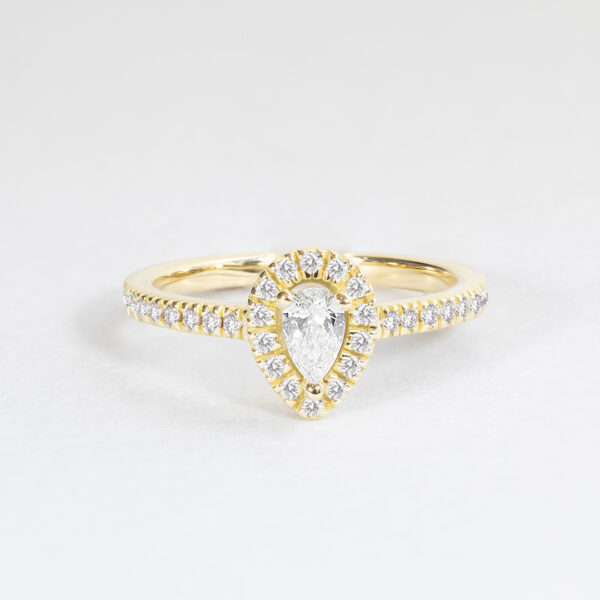 Bague en or jaune ornée d'un diamant en forme de poire, entouré de petits diamants ronds en pavé, créant un élégant design classique. Cette bague est parfaite comme bague de fiançailles ou bijou de luxe, mettant en avant le charme et l'éclat du diamant central tout en ajoutant une touche de brillance grâce à sa finition raffinée.