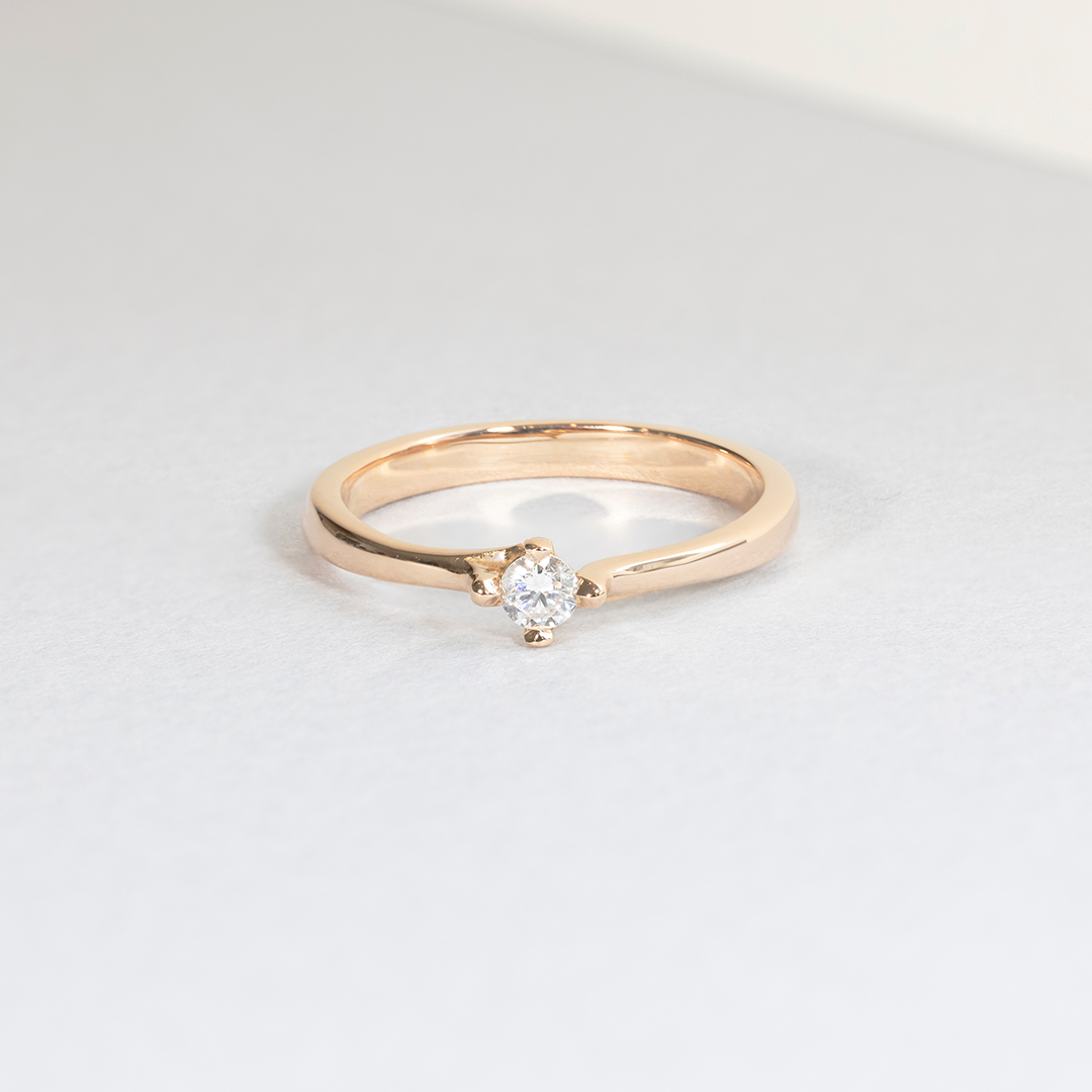 Bague en or rose avec un magnifique diamant central, mettant en valeur une élégante conception minimaliste. Idéale pour les fiançailles ou comme bijou précieux, mettant en avant la qualité artisanale d'une pièce de joaillerie raffinée.