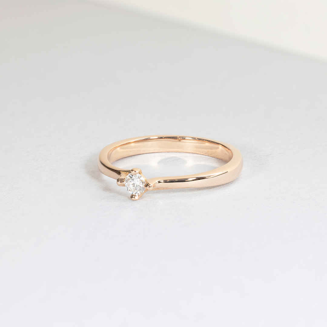 Bague en or rose élégante avec un diamant brillant au centre, stylisée avec un design minimaliste et moderne. Cette bague parfaite pour une demande en mariage, une occasion spéciale ou comme bijou intemporel est idéale pour les amateurs de bijoux raffinés. Modèle + diamant.