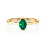 Bague en or jaune élégante avec une gemme précieuse verte en forme ovale, mettant en valeur un design moderne et chic, idéale pour les fiançailles ou les occasions spéciales, représentant le luxe et la beauté intemporelle.