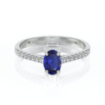 Bague en or blanc ornée d'un saphir oval bleu au centre, entourée de pierres scintillantes, modèle élégant et raffiné, parfaite pour une demande en mariage ou un cadeau spécial, ajoutant une touche de luxe à toute tenue.