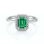 Bague en or blanc ornée d'une émeraude taille émeraude entourée de petits diamants. Ce bijou élégant allie la beauté de la pierre précieuse verte à la brillance des diamants, idéal pour une proposition de mariage ou un cadeau spécial. Design moderne et intemporel, parfait pour ajouter une touche de luxe à toute occasion.