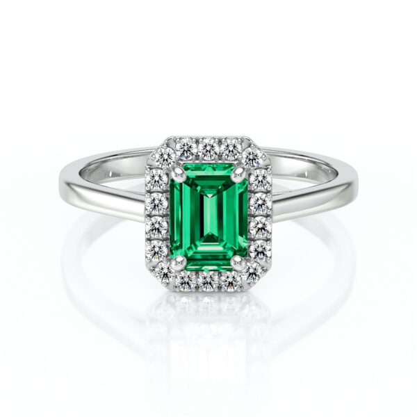 Bague en or blanc ornée d'une émeraude taille émeraude entourée de petits diamants. Ce bijou élégant allie la beauté de la pierre précieuse verte à la brillance des diamants, idéal pour une proposition de mariage ou un cadeau spécial. Design moderne et intemporel, parfait pour ajouter une touche de luxe à toute occasion.