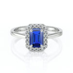 Bague en or blanc avec un saphir émeraude central de couleur bleu vif entouré de diamants scintillants. Ce bijou élégant incarne le luxe et le raffinement, parfait pour des occasions spéciales ou en tant que bague de fiançailles. Design classique et intemporel avec une finition brillante.