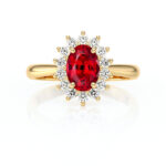 Bague en or jaune ornée d'un rubis ovale central, entouré de diamants étincelants. Ce modèle élégant allie luxe et sophistication, idéal pour des occasions spéciales ou comme bijou de fiançailles.