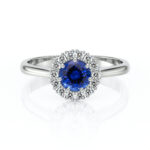 Bague en or blanc avec une pierre centrale en saphir bleu entourée de diamants scintillants, modèle élégant et raffiné, idéale pour fiançailles ou occasions spéciales, mettant en valeur le luxe et le style.