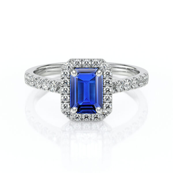 Bague en or blanc ornée d'un saphir bleu émeraude au centre, entouré d'un halo de diamants scintillants. Cette pièce élégante présente une monture délicate avec un pavé de diamants sur le corps de la bague, idéale pour une demande en mariage ou comme bijou de luxe. Modèle + diamant.