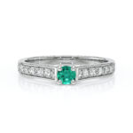 Bague en diamant et émeraude modèle élégant, présentant une pierre centrale en émeraude ronde entourée de diamants scintillants sur le band. Idéal pour les fiançailles ou comme bijou de luxe, cette bague met en avant un design raffiné et moderne, évoquant l'amour et l'exclusivité.