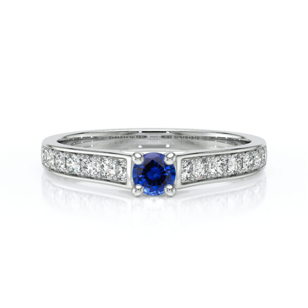 Bague en or blanc ornée d'une pierre précieuse saphir bleu centrale, entourée de diamants scintillants sur le bandeau. Élégante et raffinée, idéale pour les fiançailles ou les occasions spéciales. Design contemporain mettant en avant le contraste entre le bleu du saphir et l'éclat des diamants.
