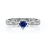 Bague en or blanc avec un diamant central bleu brillant entouré de petits diamants, design élégant et moderne, modèle de bijou parfait pour les fiançailles ou les occasions spéciales, scintillement captivant sur un fond blanc