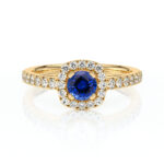 Bague en or avec un diamant central bleu, entourée de diamants scintillants sur un anneau délicat. Idéale pour les fiançailles ou comme bijou de luxe, cette bague allie élégance et sophistication, mettant en valeur la pierre précieuse au centre et le travail artisanal de haute qualité.