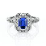 Bague en or blanc ornée d'une pierre précieuse en saphir bleu de taille émeraude, entourée de diamants scintillants, mettant en valeur un design élégant et moderne, idéale pour des fiançailles ou comme bijou de luxe.