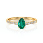 Bague en or avec une pierre précieuse en forme de poire, de couleur verte, sertie au centre, accompagnée de diamants scintillants sur le bandeau, symbolisant l'élégance et le luxe, parfaite pour un engagement ou une occasion spéciale.