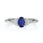 Bague en or blanc ornée d'un saphir oval bleu au centre, entouré de trois diamants brillants, idéale pour une proposition de mariage ou une occasion spéciale. Bague de fiançailles élégante avec un design moderne, mettant en valeur la beauté du saphir et l'éclat des diamants, parfaite pour les amateurs de bijoux raffinés.