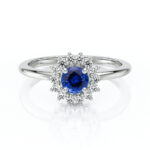 Bague de fiançailles en or blanc ornée d'un saphir bleu en forme de fleur entouré de diamants brillants. Cette pièce unique incarne l'élégance et la sophistication, parfaite pour symboliser un amour éternel. Modèle contemporain avec design floral, idéale pour les demandes en mariage.