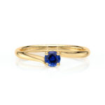 Bague en or avec un design élégant et moderne, mettant en valeur un saphir bleu taille ronde au centre, entouré de griffes dorées. Idéale pour une proposition de mariage ou un cadeau spécial, ajoutant une touche de luxe et d'originalité à toute collection de bijoux.