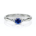 Bague en or blanc avec un saphir bleu central entouré de diamants, illustrant l'élégance et le luxe, parfait pour des fiançailles ou une occasion spéciale.