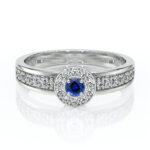 Bague en argent avec un saphir bleu central entouré de diamants, modélisée avec soin pour un éclat maximal, parfaite pour une demande en mariage ou une occasion spéciale. Design élégant avec détails sur les côtés.